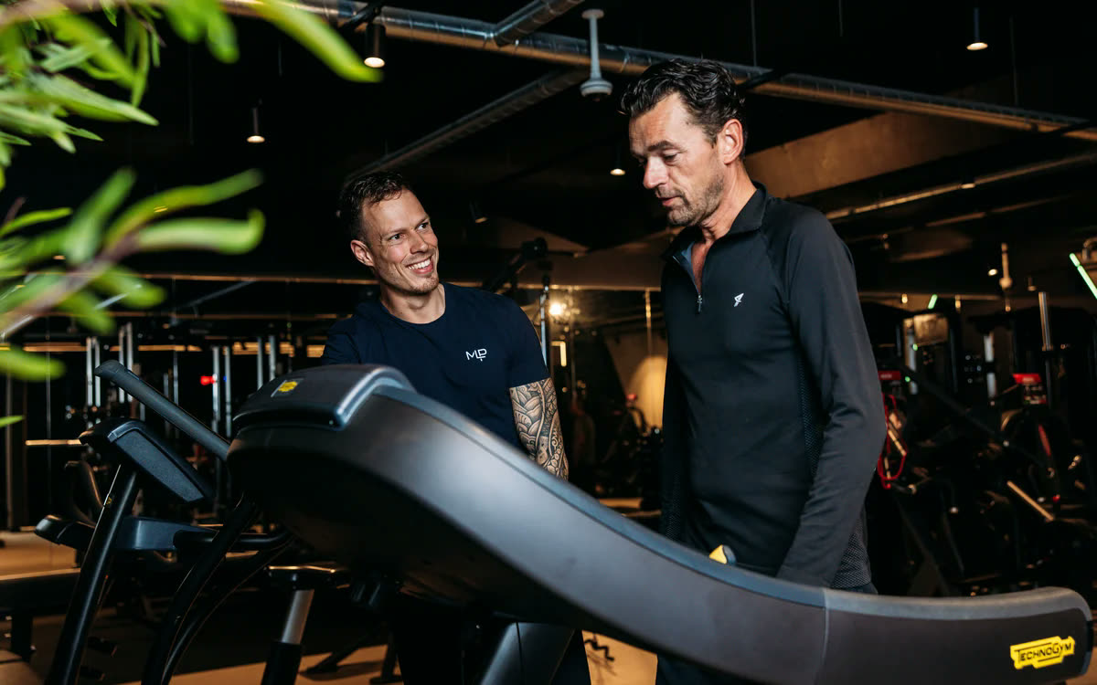 Een coach en een lid in gesprek bij een loopband
