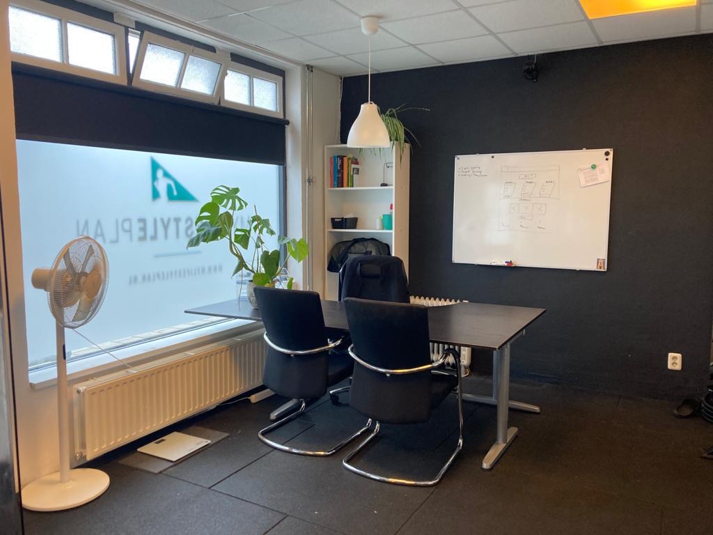 De intakeruimte van de eerste studio, met een tafel, twee stoelen en een whiteboard